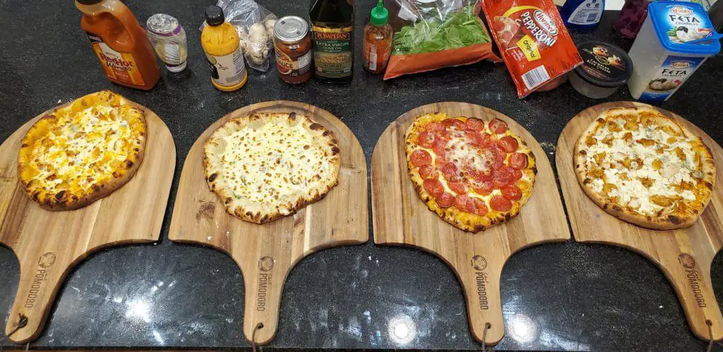 Four pizzas cooked and displayed on the Chef Pomodoro Acacia Wood Pizza Peels