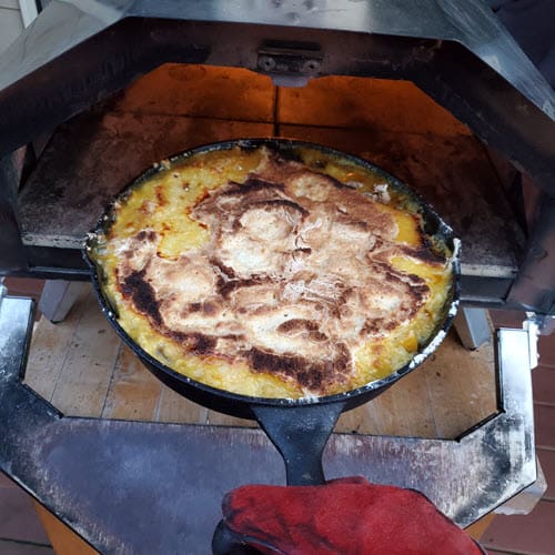 Peach Cobbler in a round cast iron skillet coming out of an Ooni Pro pizza oven