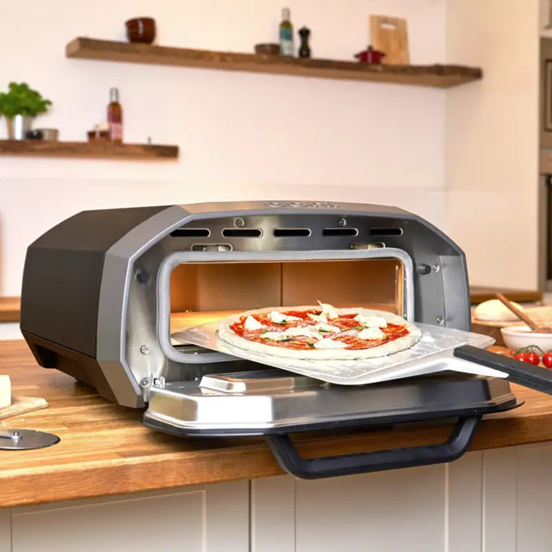 Ooni Volt 12 electric pizza oven lifestyle image with a metal peel launching a pizza. 